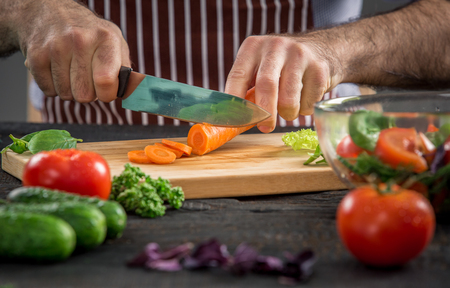 Close up on male hands cutting carrot, making salad. Chef cutting vegetables. Healthy lifestyle, diet foodの写真素材
