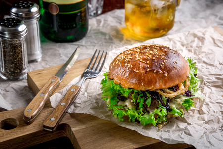 Sandwich with ostrich burger, onion, sauce and lettuce. Burger is on the table with paper and salt and pepper shakersの写真素材