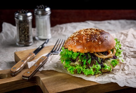 Sandwich with ostrich burger, onion, sauce and lettuce. Burger is on the table with paper and salt and pepper shakersの写真素材