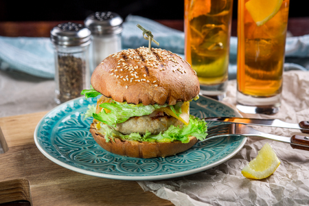 Sandwich with chicken burger, cheese and lettuce. Burger is on the table with paper and salt and pepper shakers. As well as two cocktails log Island Icedの写真素材