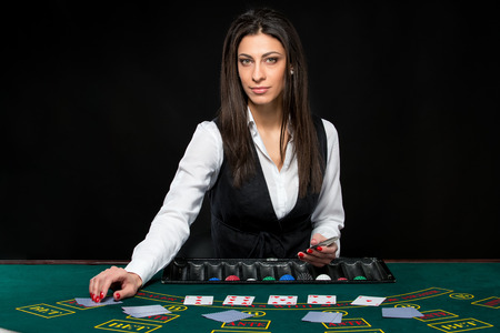 The beautiful girl, dealer, behind a table for game in poker. the dealer deals the cards. She is looking at the cameraの写真素材