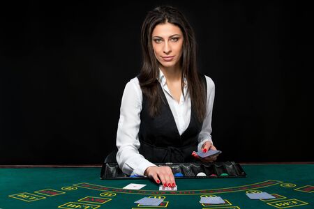 The beautiful girl, dealer, behind a table for game in poker. the dealer deals the cards. She is looking at the cameraの写真素材