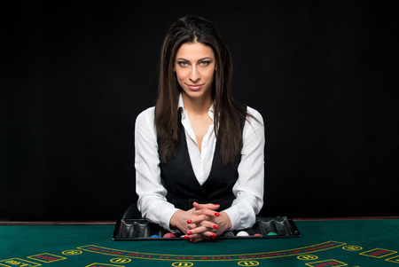The beautiful girl, dealer, behind a table for game in poker. She is looking at the camera