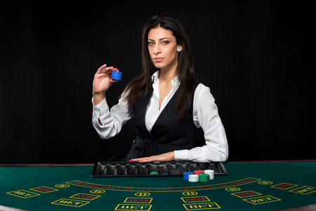 The beautiful girl, dealer, behind a table for game in poker, hold chips in handsの写真素材