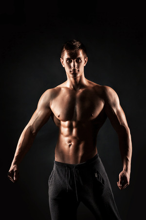 Sexy shirtless bodybuilder posing and looking at camera on black background. Extreme strength, muscles and fitness..の写真素材