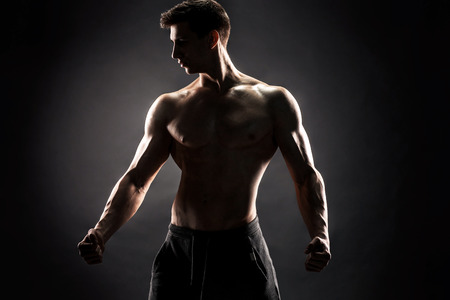 Sexy muscular man posing with naked torso in studio and looking behind on black background.の写真素材