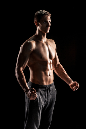 Sexy muscular man posing with naked torso in studio and looking behind on black background.の写真素材