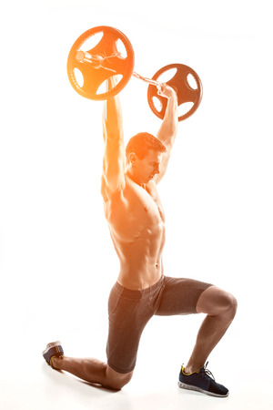 Muscular mighty man standing on knee and holding barbell over his head. Isolated on white background. Whith solar flareの写真素材