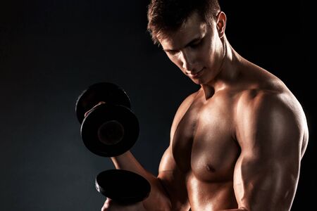 Mighty fitness man showing his gread body with dumbbells in hand on black background..の写真素材