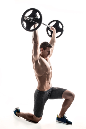 Muscular mighty man standing on knee and holding barbell over his head. Isolated on white background.の写真素材