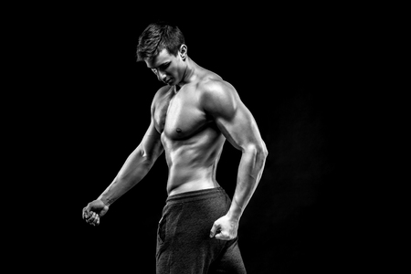 Image of very muscular man posing with naked torso in studio and looking behind on black background. Black and whiteの写真素材