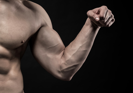 Image of very muscular man posing with naked torso in studio and looking behind on black background. Close upの写真素材