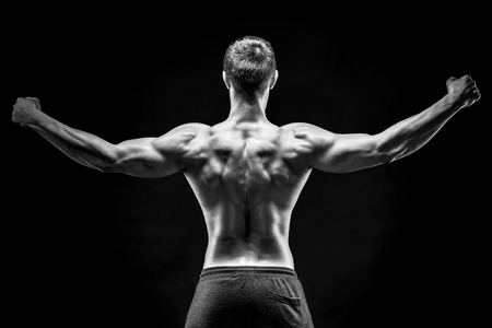Rear view of healthy muscular young man showing back, perfect shoulders, biceps, triceps on black background. Black and whiteの写真素材