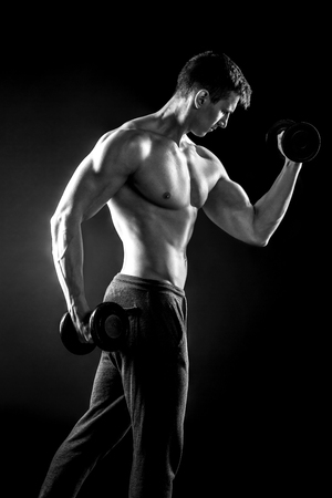 Athletic man showing muscular body and doing exercises with dumbbells on black background.. Black and whiteの写真素材