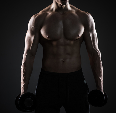 Muscular man showing perfect body with dumbbells and looking into the distance on black background. close upの写真素材