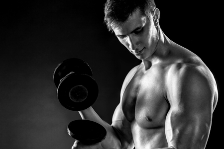 Mighty fitness man showing his gread body with dumbbells in hand on black background.. Black and white. Close upの写真素材