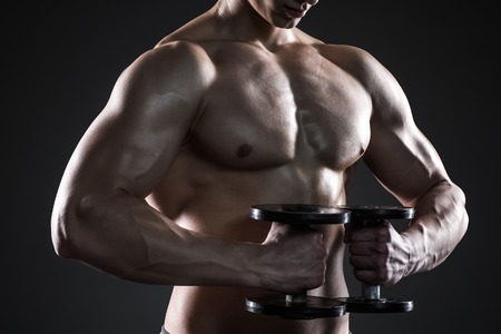 Mighty fitness man showing his gread body with dumbbells in hand on black background. Close upの写真素材