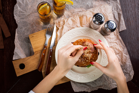 First person view of a woman preparing eat burger. Women's hands hold a knife and fork. tasty burger on a plate lyingの写真素材