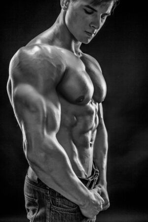 Muscular bodybuilder guy doing posing over black background. Naked torso in jeans. Close-up. Black and white, b wの写真素材