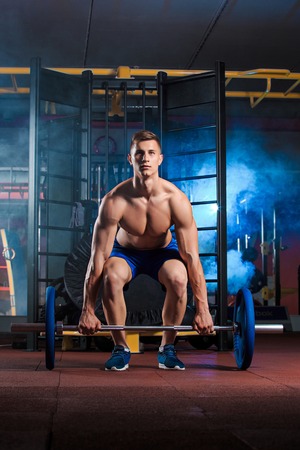 young man doing exercises with barbell in gymの写真素材