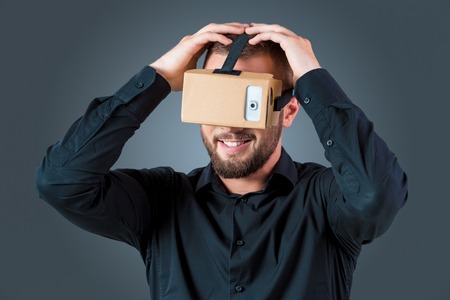 Excited young man using a VR headset glasses and experiencing virtual reality on grey blue backgroundの写真素材