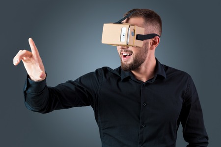 Excited young man using a VR headset glasses and experiencing virtual reality on grey blue...