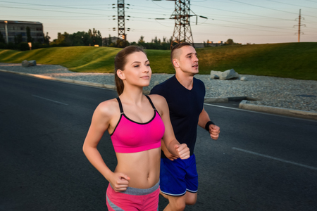 Close-up portrait of athletic couple running on the road, muscular build young runners working out while jogging in the park. Eveningの写真素材