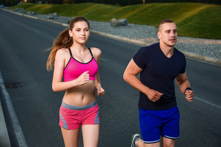 Close-up portrait of athletic couple running on the road, muscular build young runners working out while jogging in the park. Eveningの写真素材
