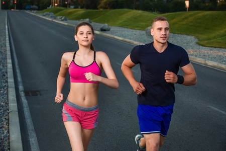 Close-up portrait of athletic couple running on the road, muscular build young runners working out while jogging in the park. Eveningの写真素材