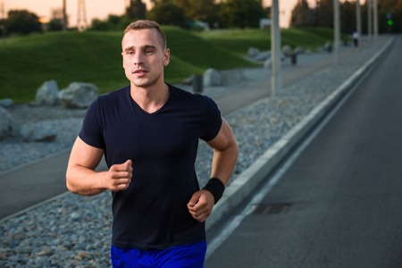 Close-up portrait of athletic man running on the road, muscular build young runner working out while jogging in the park. Eveningの写真素材
