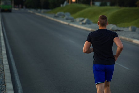 Close-up portrait of athletic man running on the road, muscular build young runner working out while jogging in the park. Evening. view from the backの写真素材