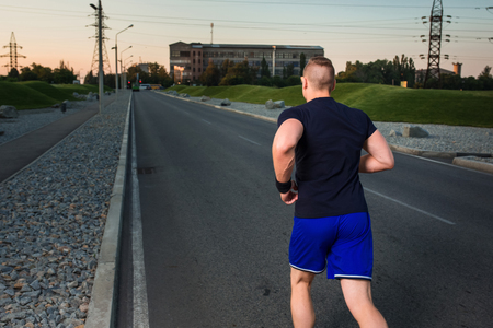 Close-up portrait of athletic man running on the road, muscular build young runner working out while jogging in the park. Evening. view from the backの写真素材