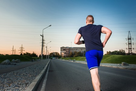 Close-up portrait of athletic man running on the road, muscular build young runner working out while jogging in the park. Evening. view from the backの写真素材
