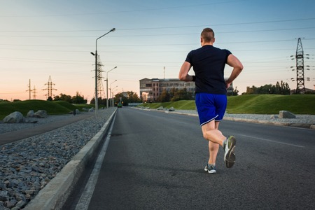 Full length portrait of athletic man running on the road, muscular build young runner working out while jogging in the park. Evening. view from the backの写真素材