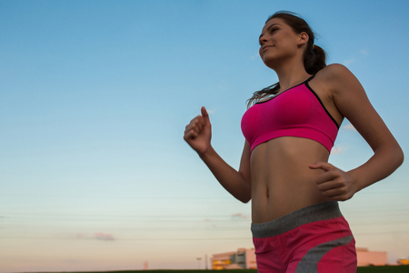 Running woman. Runner jogging in sunny nature. Female fitness model training outside in sunset sky background.の写真素材