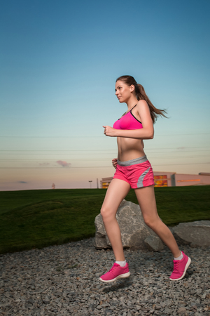 Running woman. Runner jogging in sunny nature. Female fitness model training outside in sunset sky background.の写真素材