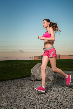Running woman. Runner jogging in sunny nature. Female fitness model training outside in sunset sky background.の写真素材