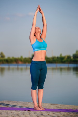 girl doing yoga exercises on the river bank at sunsetの写真素材