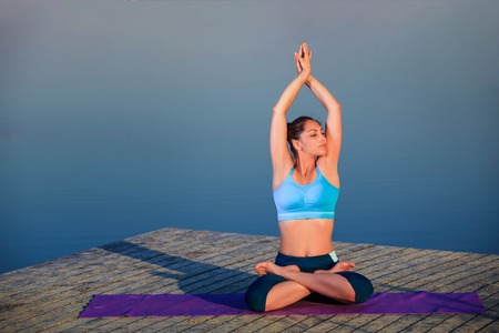 girl doing yoga exercises on the river bank at sunset. copyspaceの写真素材