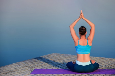 girl doing yoga exercises on the river bank at sunset. copyspaceの写真素材