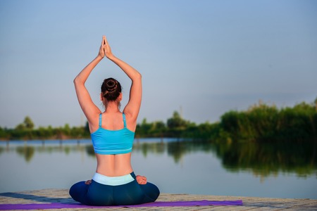 girl doing yoga exercises on the river bank at sunset. copyspaceの写真素材