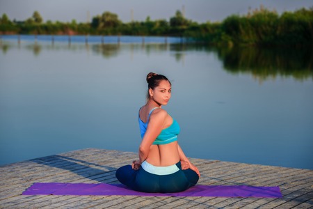 girl doing yoga exercises on the river bank at sunsetの写真素材