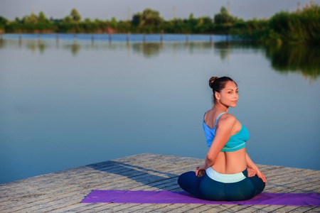 girl doing yoga exercises on the river bank at sunset. copyspaceの写真素材