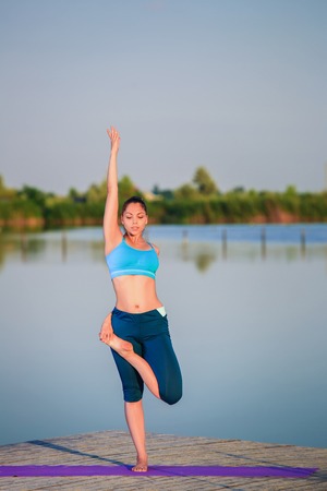girl doing yoga exercises on the river bank at sunsetの写真素材