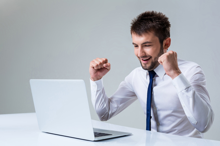 young man smiling and enjoys uses a laptop computer while sitting at a table. Office clothingの写真素材