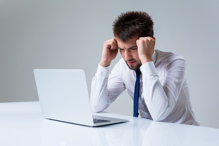 young man frustrated using laptop computer sitting at the table. Office clothingの写真素材