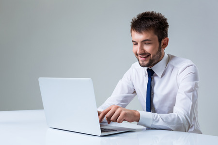 young man smiling and typing using laptop computer sitting at the table. Office clothingの写真素材