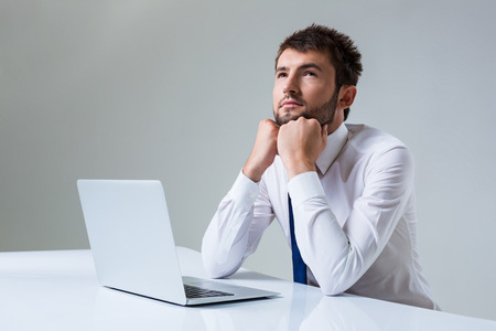 young man thinking uses a laptop computer while sitting at a table. Office clothingの写真素材