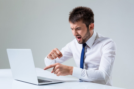 the young man is nervous and poke a finger. It uses a computer while sitting at a table. Office clothingの写真素材