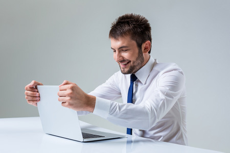 young man smiling and typing using laptop computer sitting at the table. Office clothingの写真素材
